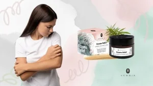Une jeune femme regarde sa peau, avec une crème contre l’eczéma à côté d’elle, logo Hemnia en bas à droite