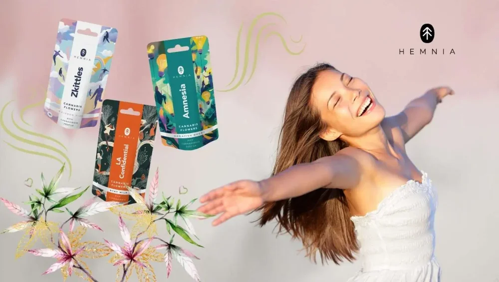 A smiling woman in a white dress is feeling the relaxing effects of CBD and next to her are packs of CBD Hemnia flowers