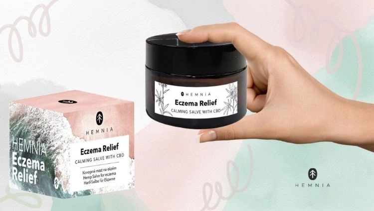 Hemnia Eczema Relief ziede sievietes ar ekzēmu rokā, blakus produkta kastītei, ar Hemnia logotipu apakšējā labajā stūrī